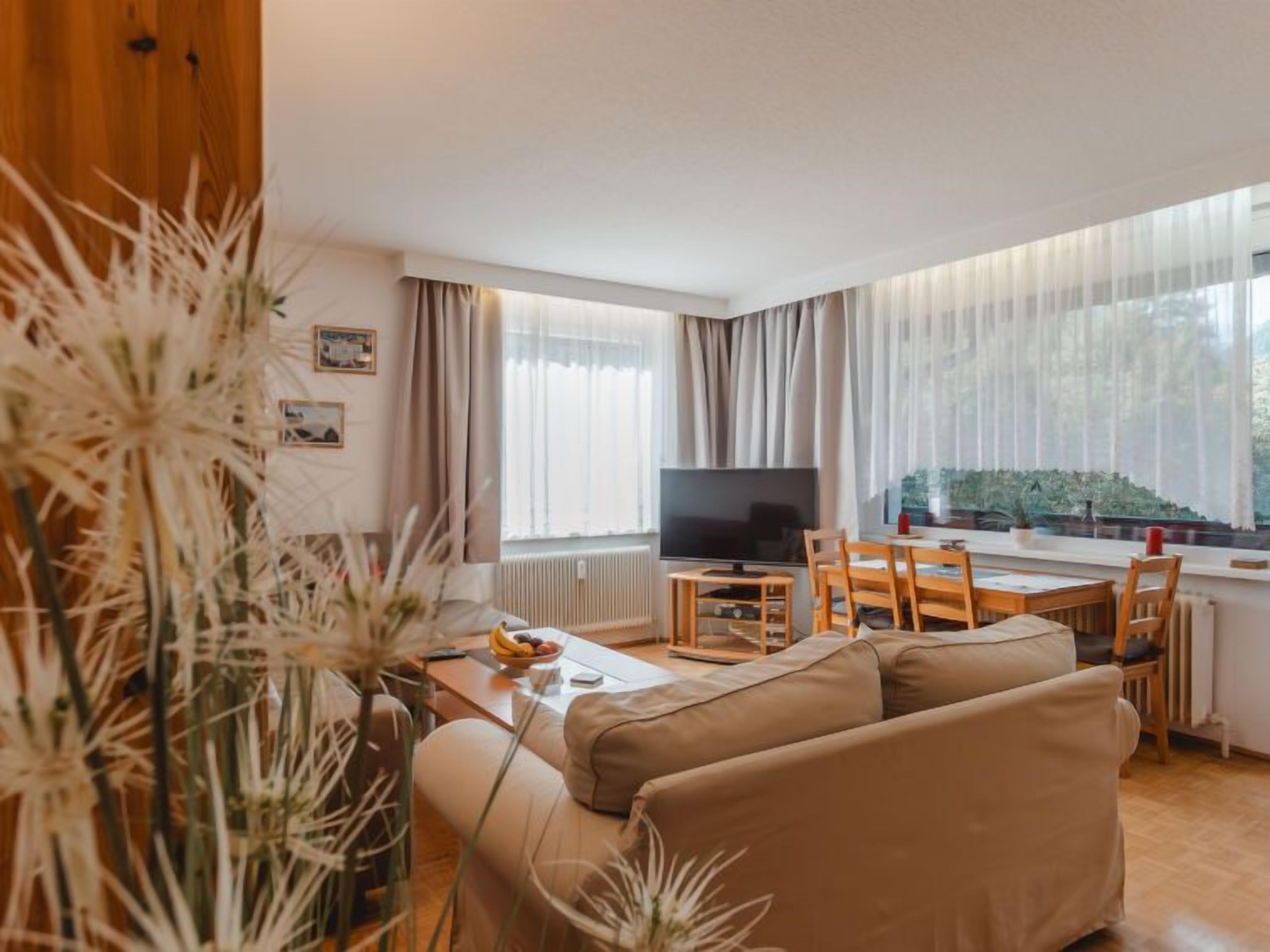 Una sala de estar con un sofá, una televisión, una mesa de comedor con sillas y un ventanal con cortinas.