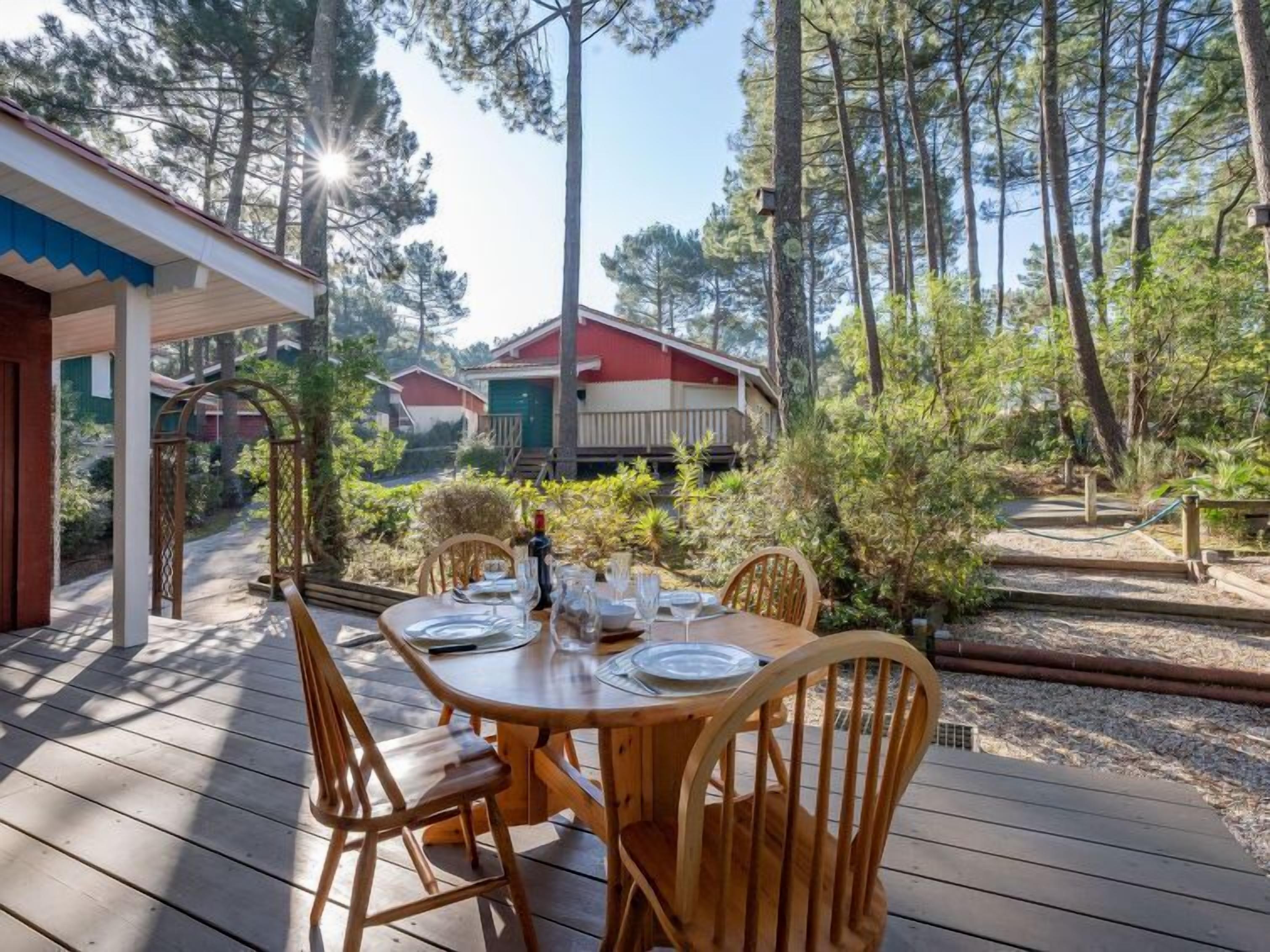 Een houten terras met een eettafel, omringd door bomen en een uitzicht op vakantiehuisjes in de verte.