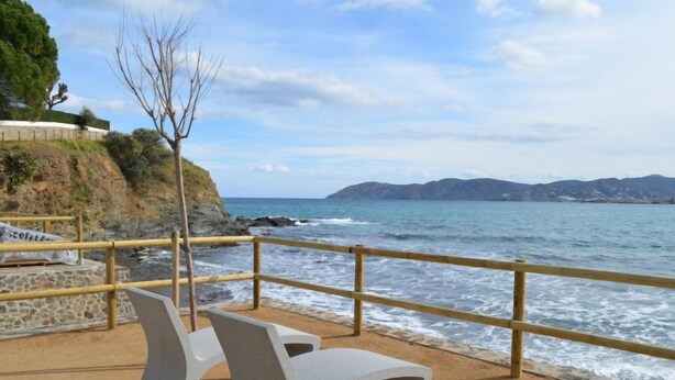 A coastal area with a sandy beach, a wooden railing, and two white benches facing the sea. - Mar Nou by Interhome (Llançà)