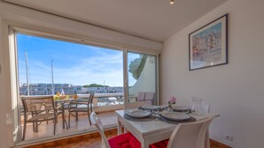 Un coin repas avec une table dressée pour deux personnes, une vue sur le port de plaisance et un tableau encadré au mur.