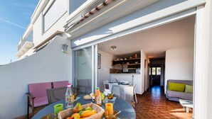 Un espace de restauration en plein air avec une table dressée pour deux personnes, un panier en osier rempli de fruits et diverses boissons.