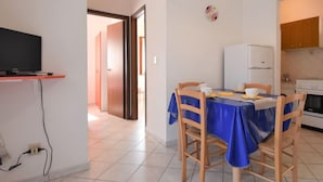 Ett kompakt bostadsutrymme med en matplats, ett litet kök och en tv som står på ett stativ.
