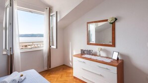 Un dormitorio con un aparador de madera, un espejo y vista al mar a través de una ventana abierta.
