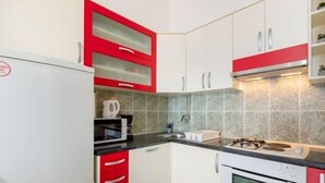 Cocina compacta con armarios blancos, detalles en rojo, estufa a gas, microondas y refrigerador.