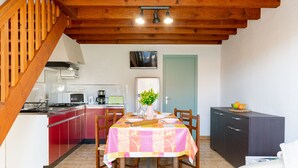 Un'accogliente cucina con zona pranzo, travi in legno al soffitto, un televisore sopra la porta e un piccolo armadietto.