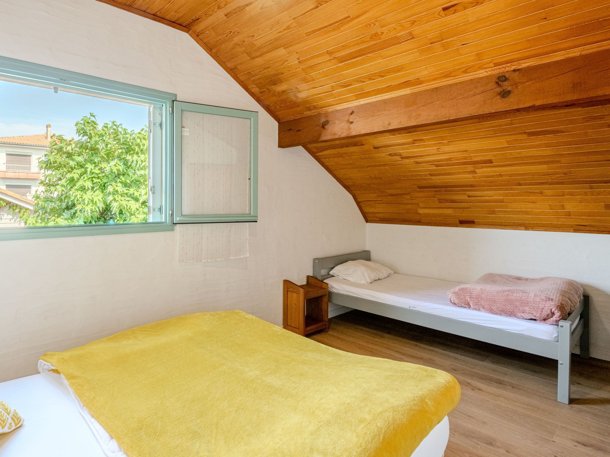 Una habitación pequeña y acogedora con techo de madera, una cama individual con una manta amarilla y una ventana que da a vistas de vegetación.