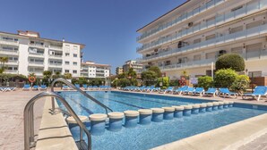 A swimming pool with blue water, surrounded by lounge chairs and a building with multiple balconies.