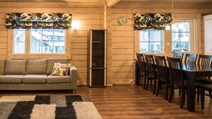 Una habitación acogedora con sofá, una mesa de comedor con sillas, un reloj en la pared y ventanas con cortinas estampadas.