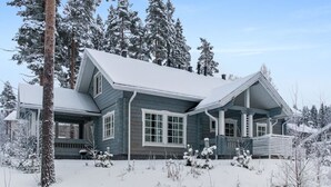 Una casa grande de dos pisos con un techo pronunciado, rodeada de árboles cubiertos de nieve y un jardín nevado.