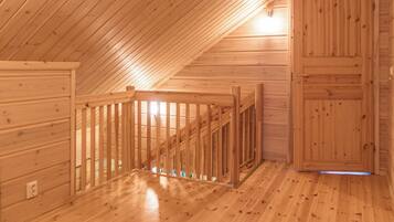 A wooden interior with a sloped ceiling, a wooden door, and a wooden railing.