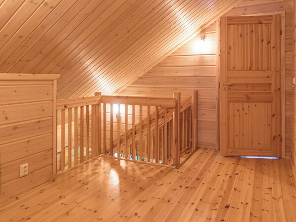 A wooden interior with a sloped ceiling, a wooden door, and a wooden railing.