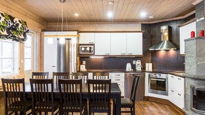 Una cocina moderna con armarios de madera, un refrigerador de acero inoxidable, un microondas y una estufa. Hay una mesa de comedor con sillas y una chimenea.