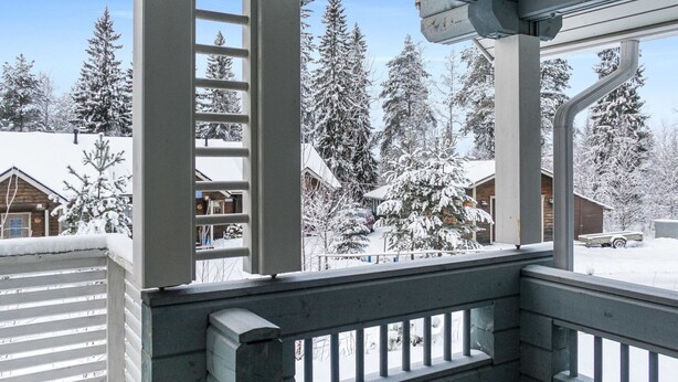 Un espacio al aire libre cubierto con barandilla de metal, árboles cubiertos de nieve y edificios al fondo.