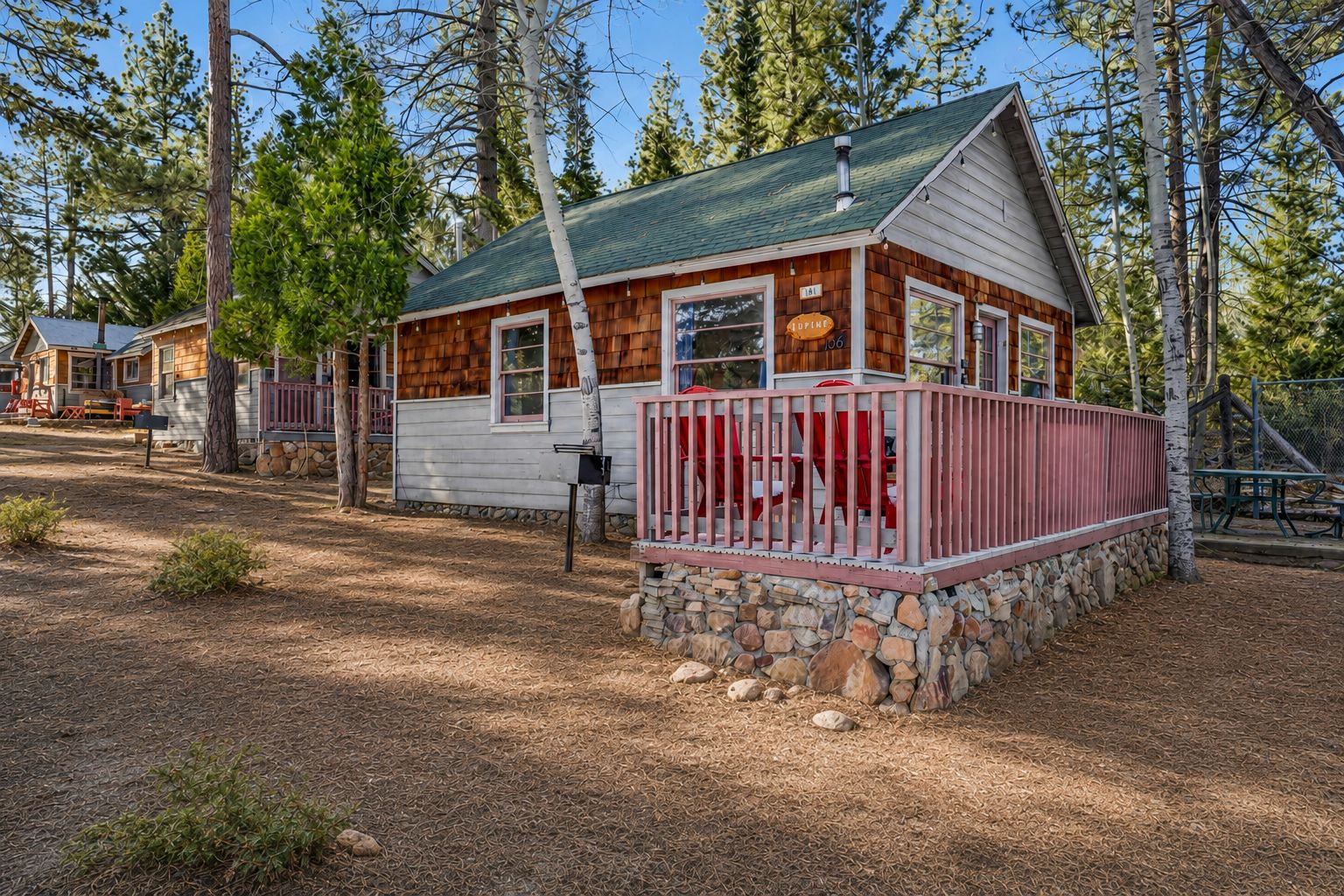 Une cabane avec des fondations en pierre, un revêtement extérieur en bois et une balustrade rouge autour de la véranda.