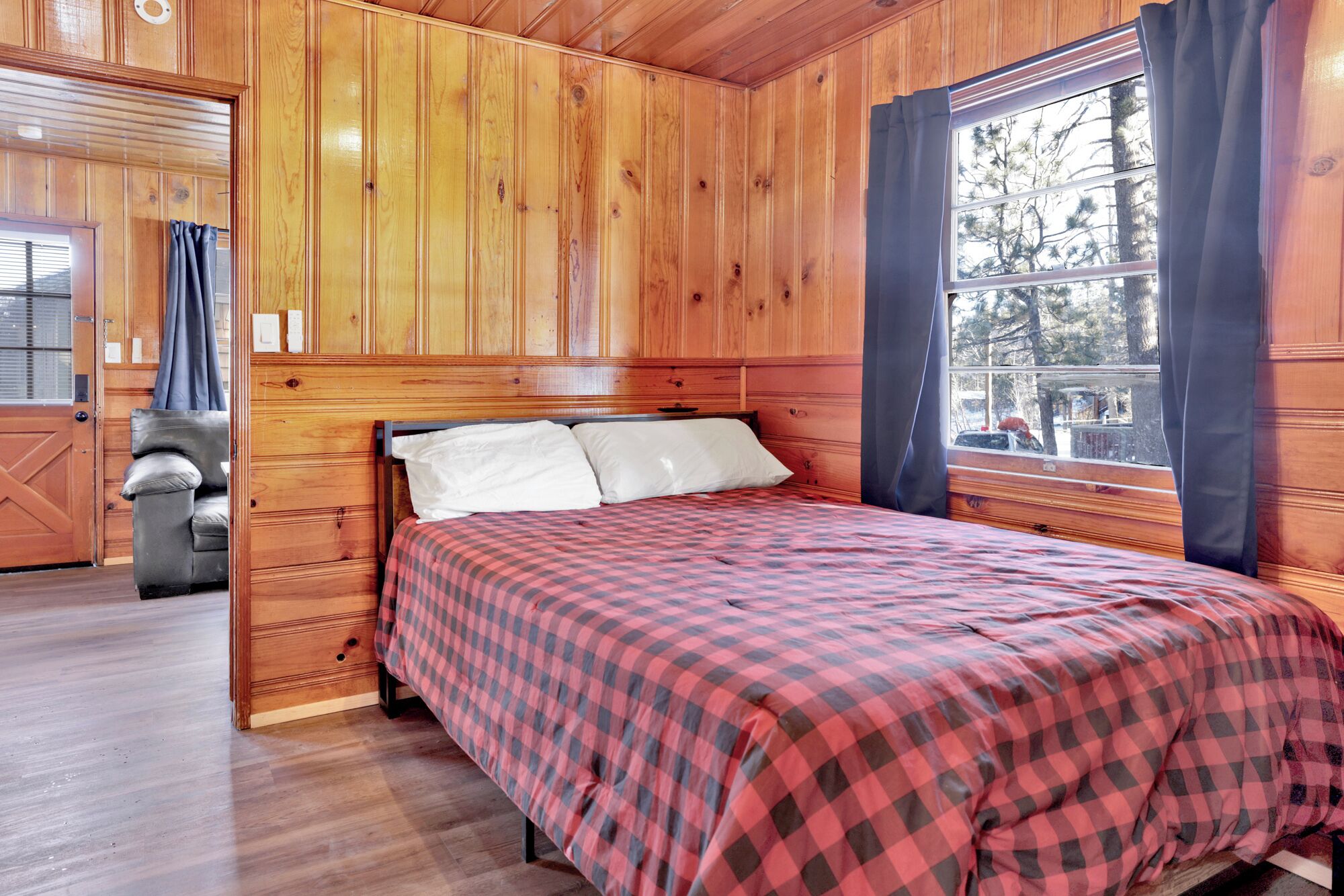 Ein Zimmer in einer Holzhütte mit einem Bett, einem Sessel und einem Fenster mit Vorhängen.