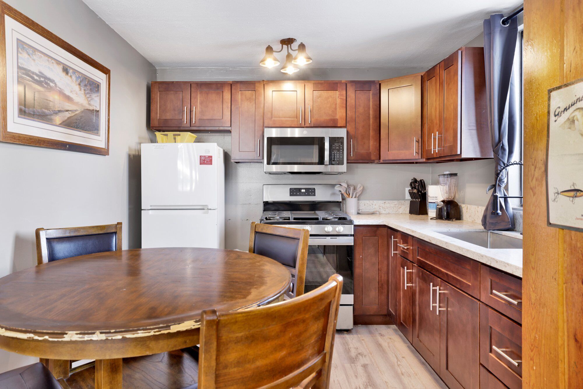 A compact kitchen with wooden cabinets, a refrigerator, a microwave, an oven, and a dining table with chairs.
