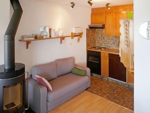 Una sala de estar acogedora con un sofá, una chimenea, armarios de madera y un salpicadero de azulejos en la cocina.