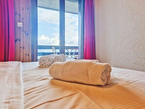 A hotel room with a bed, two rolled towels, a window with a view of mountains, and wooden walls. - Foret E3 by Interhome (Nendaz)