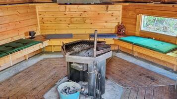 A wooden interior with a central cooking area, benches, and a window.