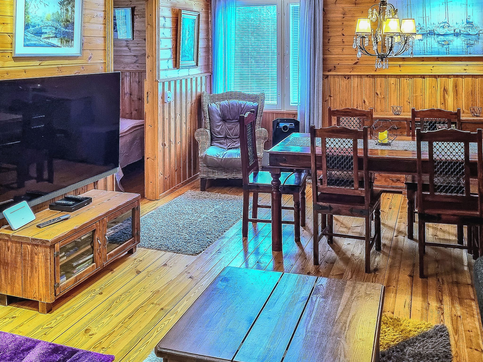 A cozy living room with a wooden floor, a sofa, a dining table with chairs, and a television.