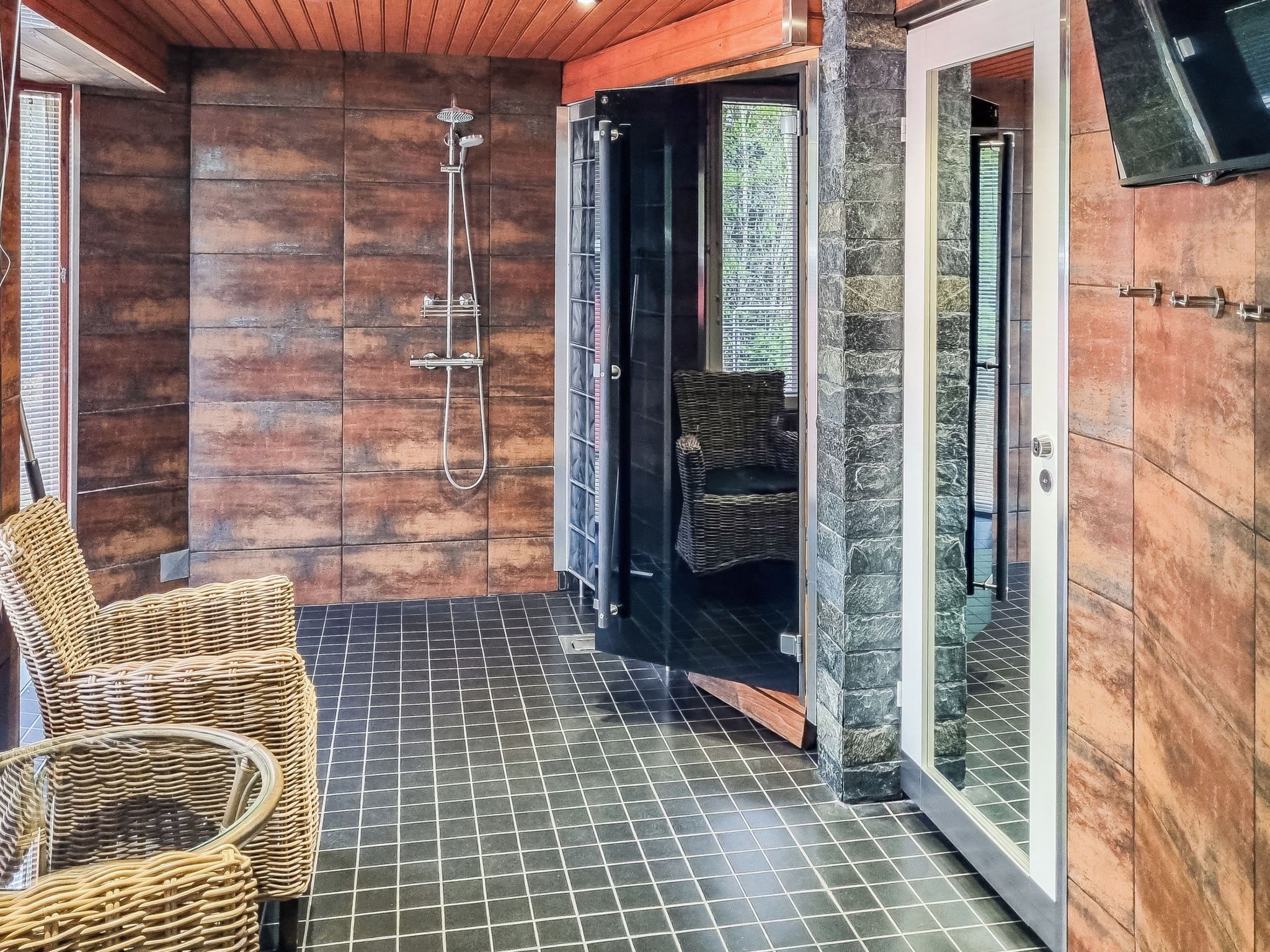 A shower area with a glass door, a wicker chair, and a tiled floor.