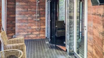 A shower area with a glass door, a wicker chair, and a tiled floor.