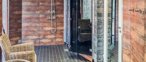 A shower area with a glass door, a wicker chair, and a tiled floor.