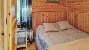 Une pièce chaleureuse avec un mur lambrissé, un lit recouvert d’une couvre-lit à motifs, une table de chevet et une fenêtre avec un rideau.