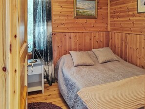 A cozy room with a wooden paneled wall, a bed with a patterned bedspread, a nightstand, and a window with a curtain.