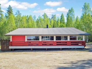 Un bâtiment d’un seul étage, à la façade rouge et au toit métallique, entouré d’une forêt.