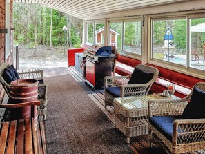 Een overdekt terras met rieten meubilair, een barbecue en uitzicht op de omgeving.