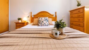 A neatly made bed with a floral pillow, a bedside table with a lamp and a plant, and a wooden dresser with a plant on top. - Res Mediterraneo by Interhome (Deltebre)