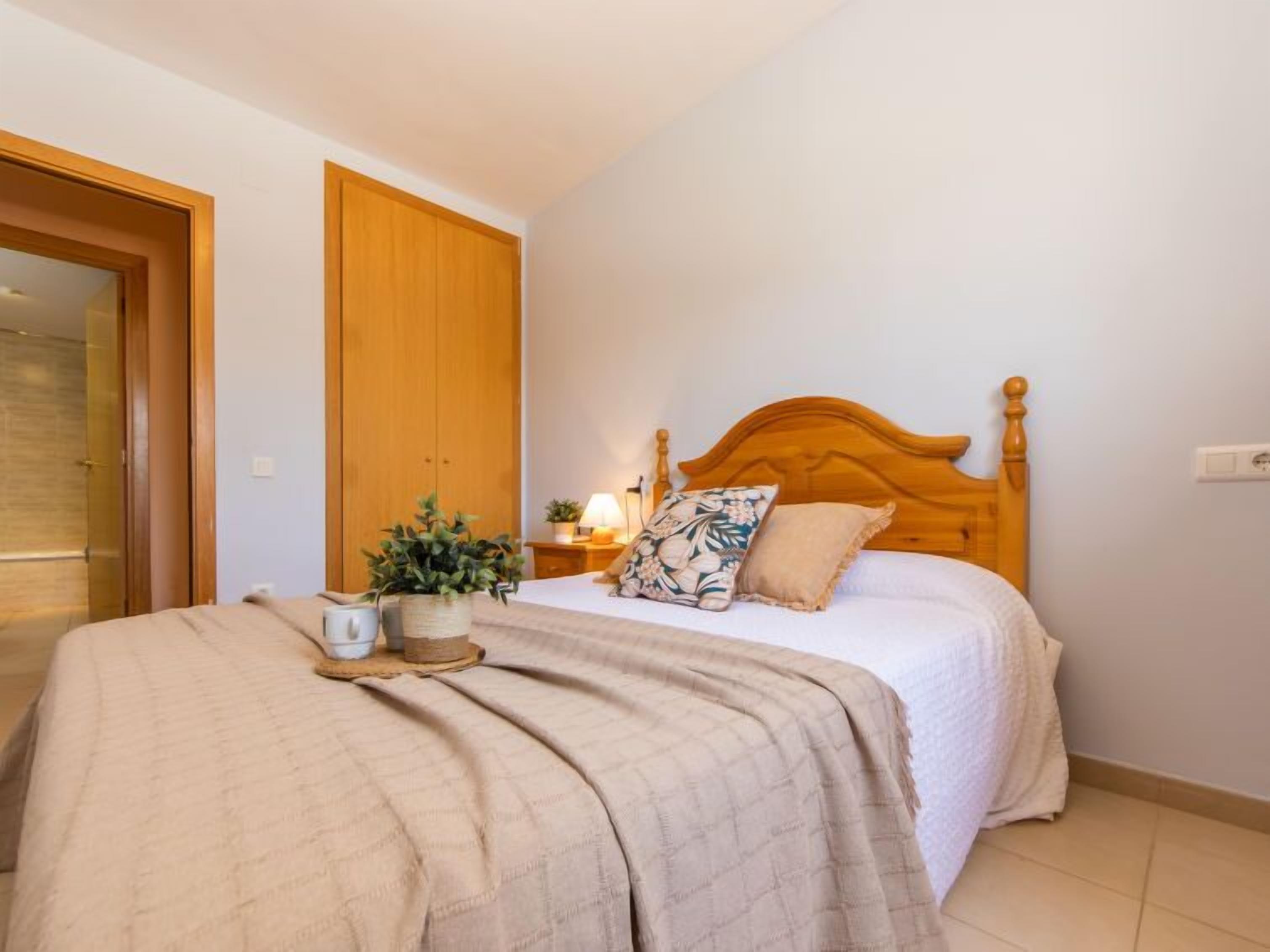 Een slaapkamer met een houten bed, een nachtkastje met een lamp, een potplant en een grote houten deur.