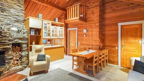 L’intérieur chaleureux d’un chalet en bois, avec une cheminée en pierre, une table à manger en bois et un coin salon confortable.