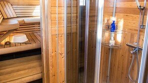 Un sauna en bois avec un banc, une porte en verre et un espace douche équipé d’un flacon de shampoing.