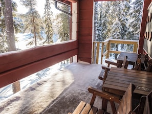 A wooden deck with a view of snow-covered trees and a clear sky.