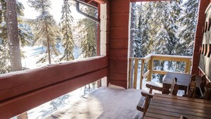 Une terrasse en bois avec une table et des chaises, donnant sur une forêt enneigée.