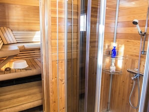 A wooden cabin interior with a sauna, a bench, and a shower area.
