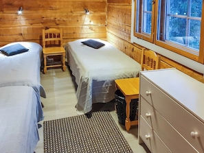 A cabin interior with two single beds, a wooden chair, a small table, and a dresser.