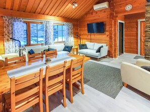 A log cabin interior with a dining area, sofa, and TV mounted on the wall.