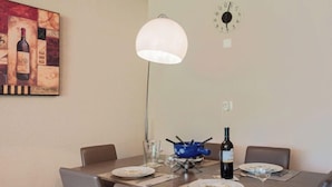 Un coin repas avec une table dressée pour deux personnes, une bouteille de vin et une horloge au mur.
