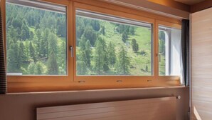 Une chambre avec une grande fenêtre donnant sur une colline boisée.