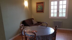 A dining area with a round table, chairs, a brown sofa, a framed artwork, and a window with blinds. - furnished apartment with all mod cons in a detached house with a garden (Bagnoles-de-l'Orne)