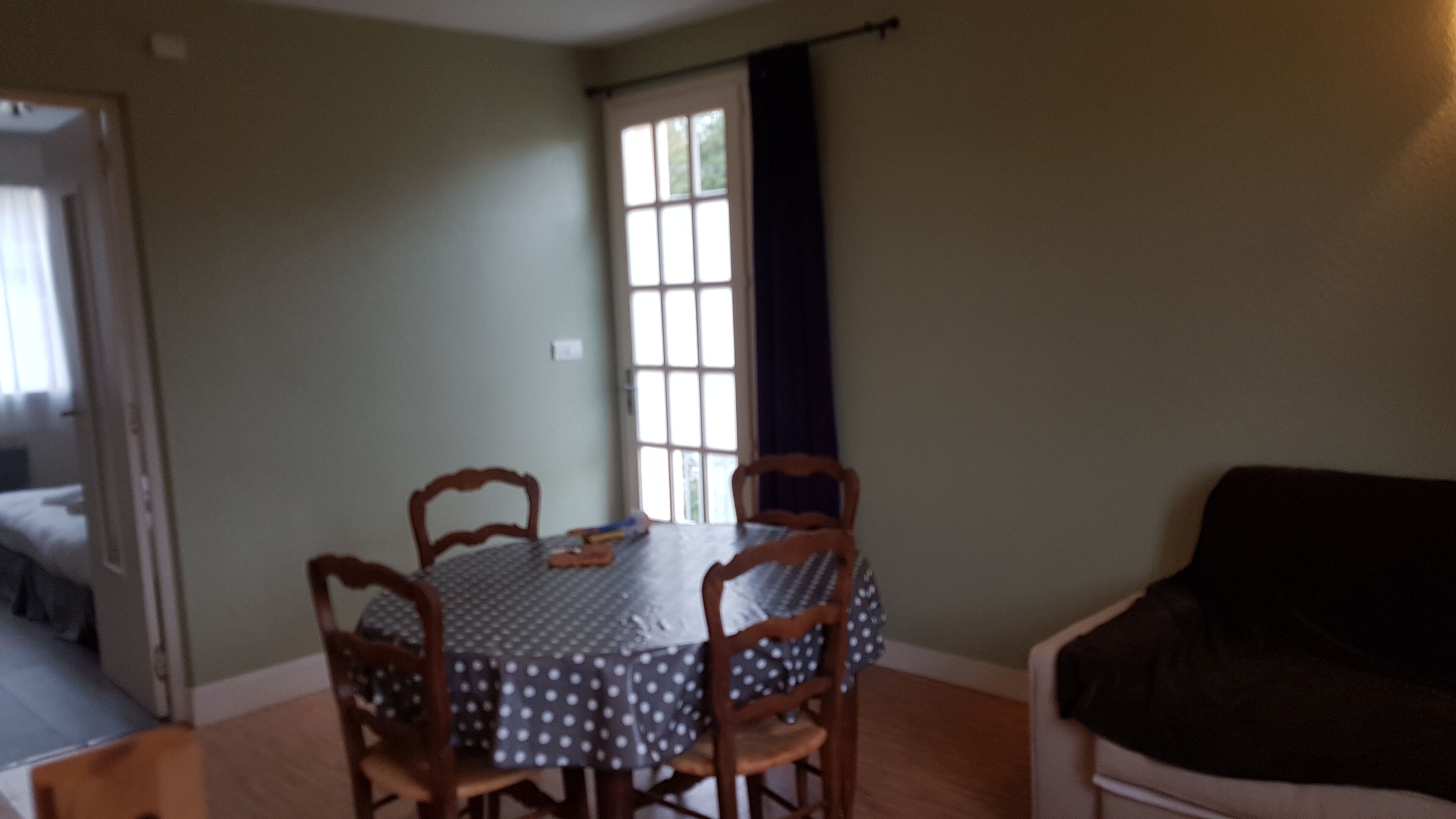 A dining area with a round table and four chairs, a window with curtains, and a dark-colored sofa.