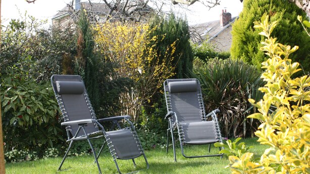 Two reclining chairs in a garden with a variety of plants and a building in the background. - furnished apartment with all mod cons in a detached house with a garden (Bagnoles-de-l'Orne)