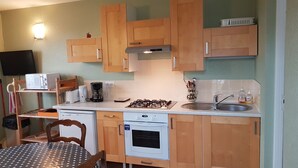 A compact kitchen with wooden cabinets, a microwave, a coffee maker, a toaster, a gas stove, and a sink. - furnished apartment with all mod cons in a detached house with a garden (Bagnoles-de-l'Orne)