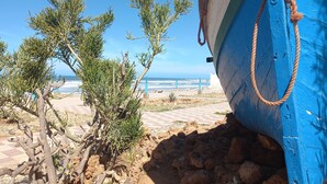A coastal scene with a blue boat, rocky terrain, and sparse vegetation. - Town house in Aglou Plage "chez Laurent": Ocean and Mountain  (Unknown)