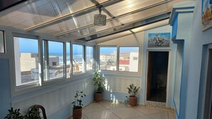 A sunlit room with large windows, potted plants, and a view of buildings. - Town house in Aglou Plage "chez Laurent": Ocean and Mountain  (Unknown)