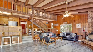 A spacious living area with a wooden staircase, a fireplace, and a large window providing a view of the outdoors.