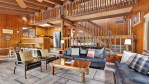 A spacious living area with a wooden staircase, leather sofas, and a kitchen in the background.